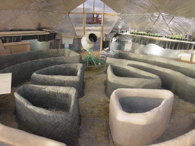 Alt text for image 4: "A variety of stucco raised beds in different shapes and sizes within a greenhouse structure, with a concrete mixer and gardening supplies in the background.