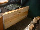 A raised garden bed crafted from rough sawn 4"x4" lumber, filled with soil and young plants, positioned inside a greenhouse with natural sunlight.