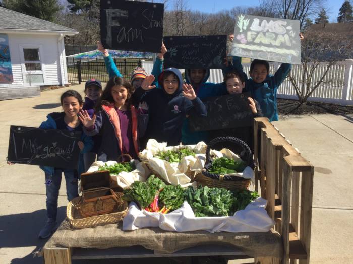 Growing Dome Community Greenhouse Farm Stand, group of kids with Farm Stand Signs behind a table of produce