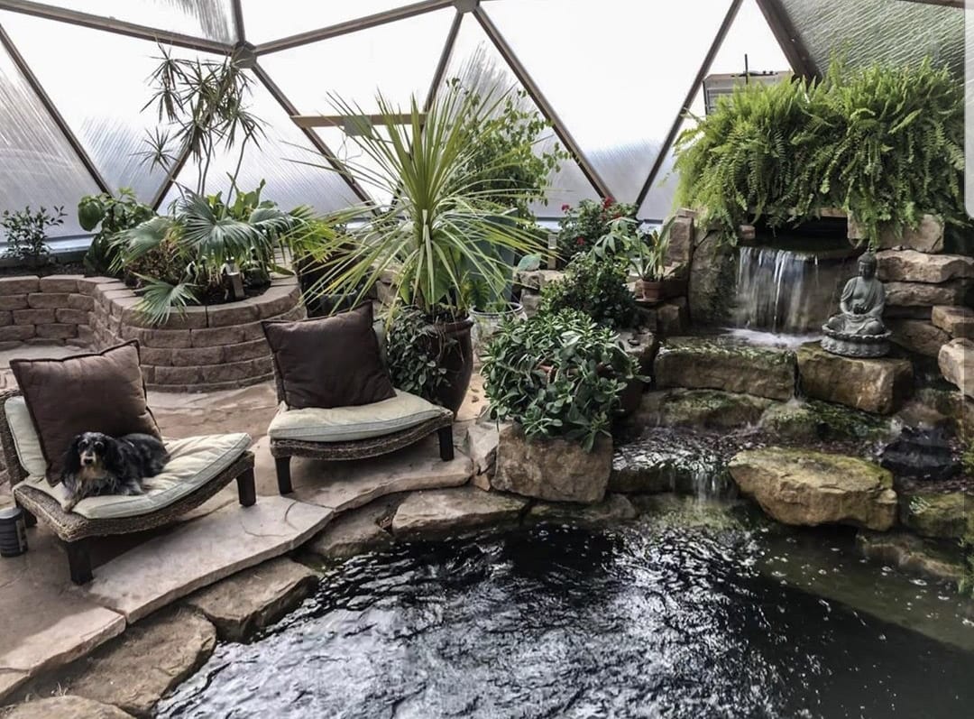 custom below-ground pond with rock waterfall and dog sitting in a chair overlooking the water