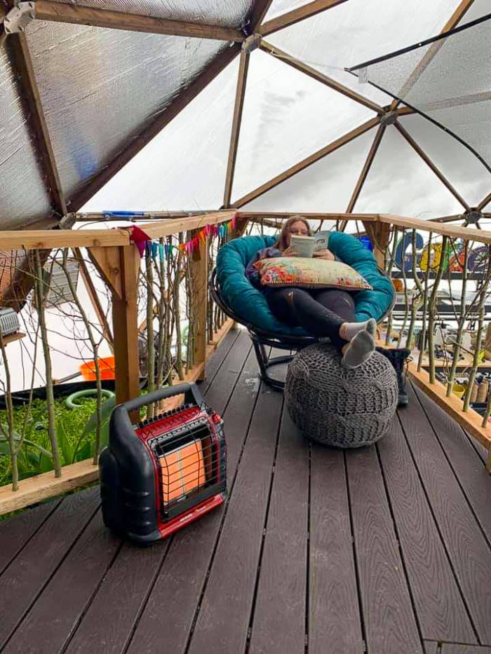 someone relaxing and reading in a chair with a space heater on the Deck above the pond in a geodesic dome