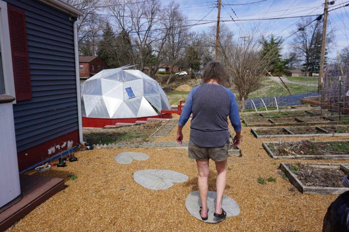 woman walking over lily pads in her yard to her dome greenhouse in souther illinois