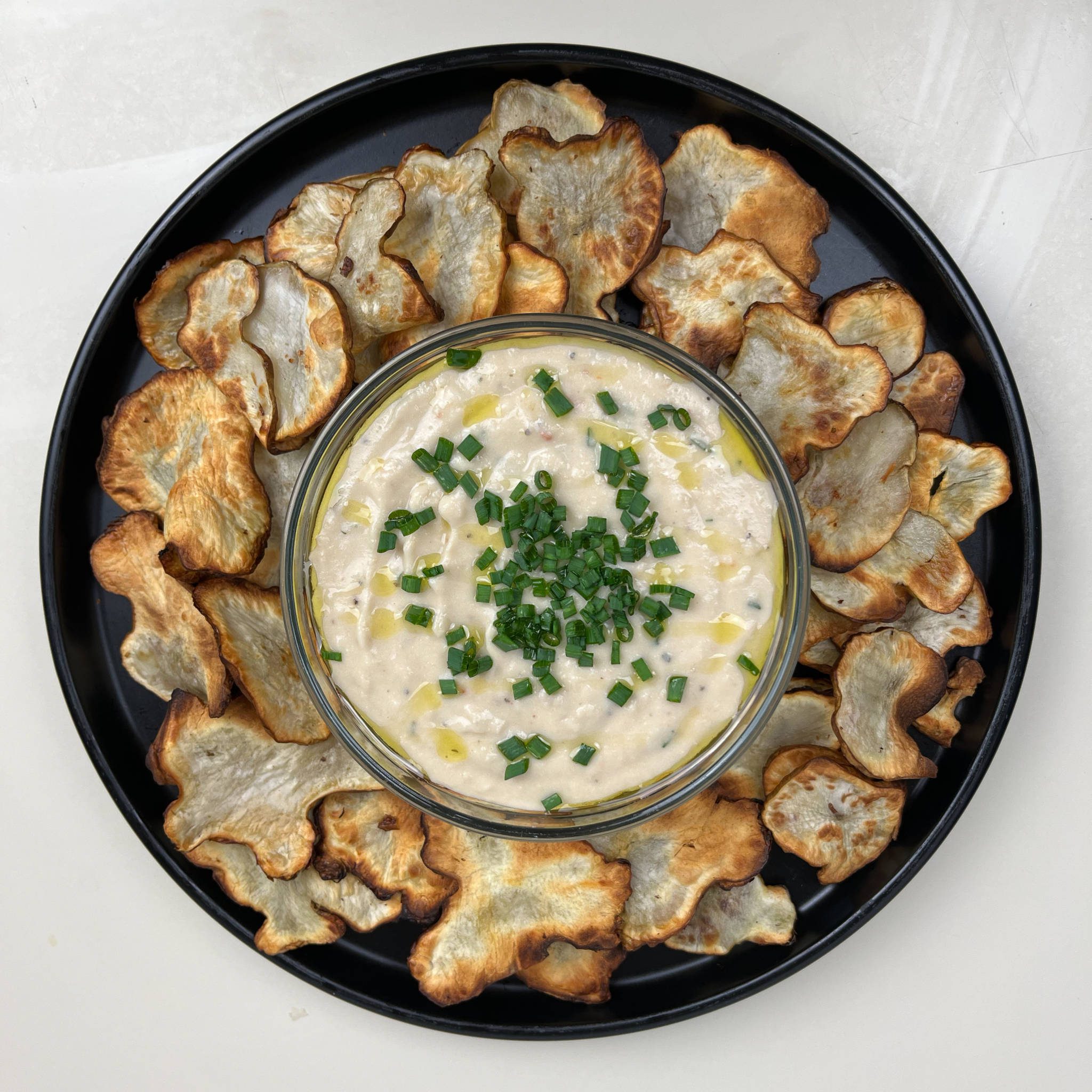 Bowl of rosemary and roasted garlic dip surrounded by sunchoke chips