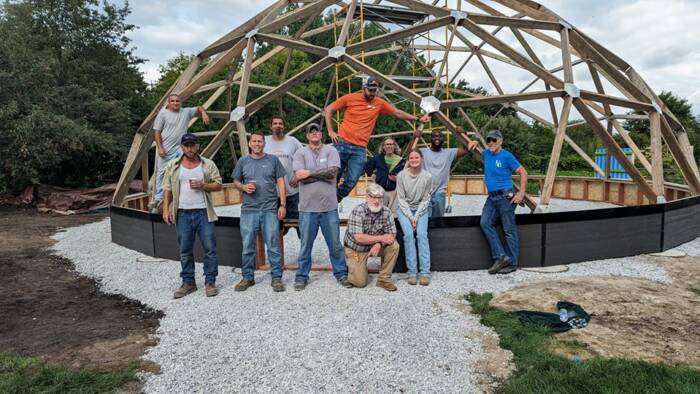 ReEntry program volunteers posing in front of heir half built dome  greenhouse as a team