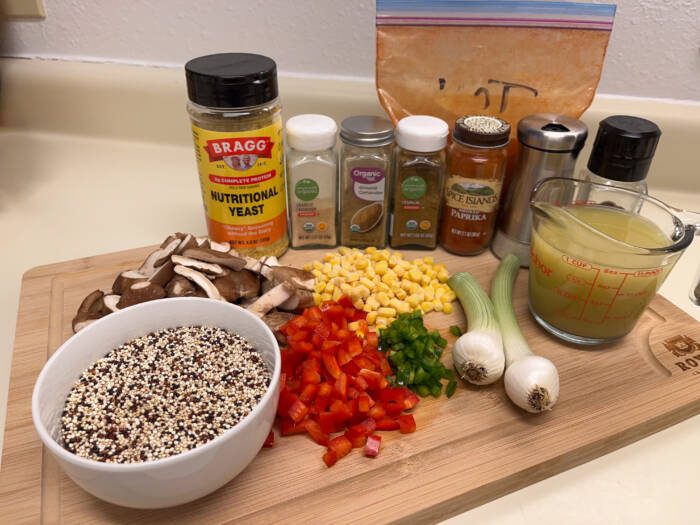 Ingredients for vegan taco meat on a cutting board: quinoa, mushrooms, bell pepper, jalapeno, corn, onions, vegetable broth, and spices