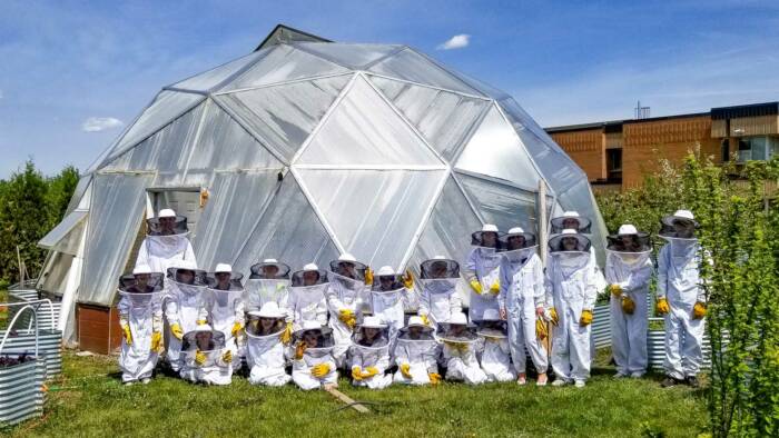 group of young beekeepers pose for a portrait all dressed in beekeeping suits and hats with a Growing Dome behind them