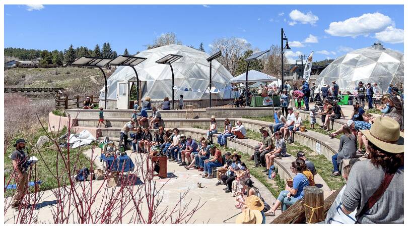 Crowd of people sitting in an amphitheater. Solar panels and two 42' Growing Domes are in the background